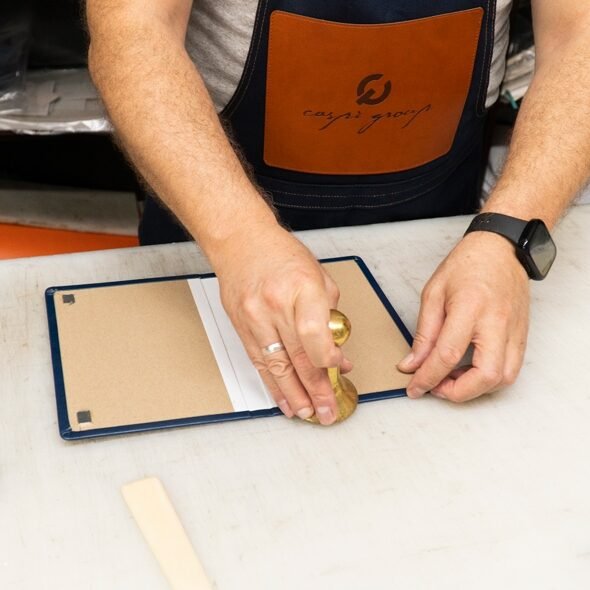 Craftsman pressing a brass die into a leather cover